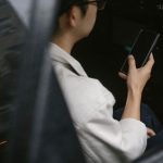 Passageiro sentado no banco traseiro de um táxi amarelo consulta informações no smartphone.