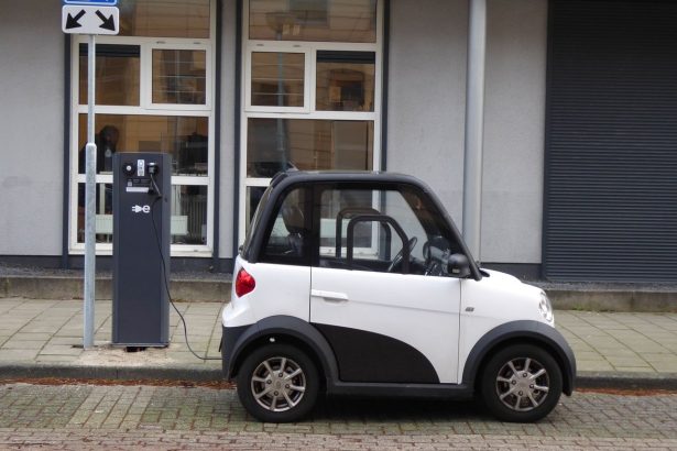 Carro compacto elétrico branco e preto conectado a uma estação pública de recarga.