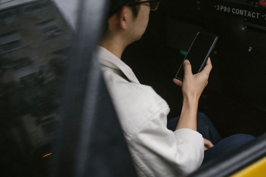 Passageiro sentado no banco traseiro de um táxi amarelo consulta informações no smartphone.