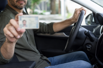 Motorista ao volante de um carro com documento de habilitação desfocado nas mãos