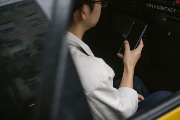 Passageiro sentado no banco traseiro de um táxi amarelo consulta informações no smartphone.