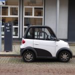 Carro compacto elétrico branco e preto conectado a uma estação pública de recarga.