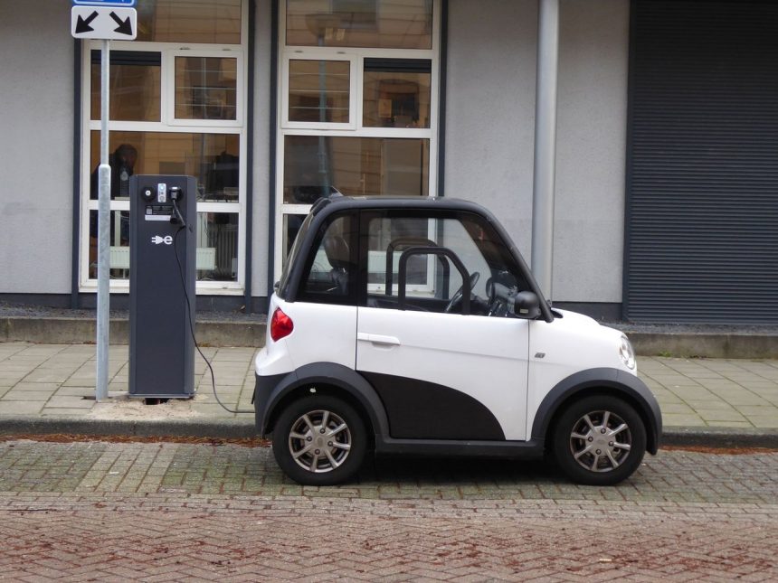 Carro compacto elétrico branco e preto conectado a uma estação pública de recarga.